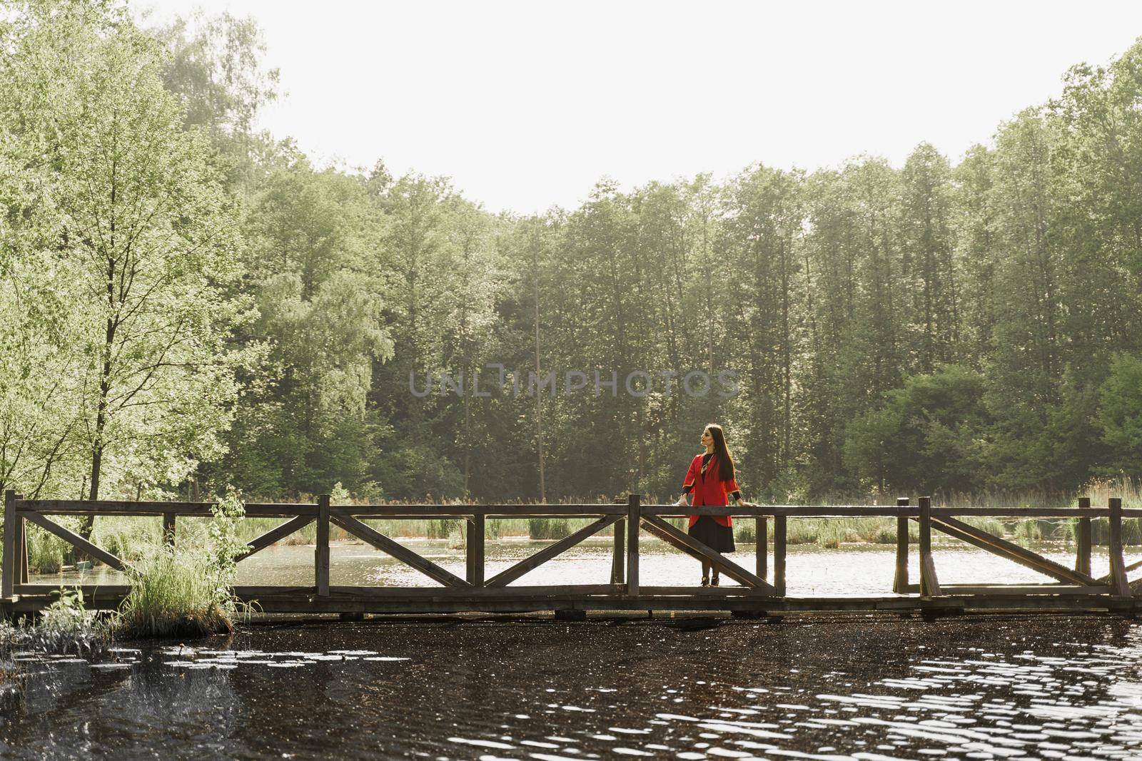 Georgian woman in red national dress with cross symbols. Attractive woman on the lake with forest background. Georgian culture lifestyle