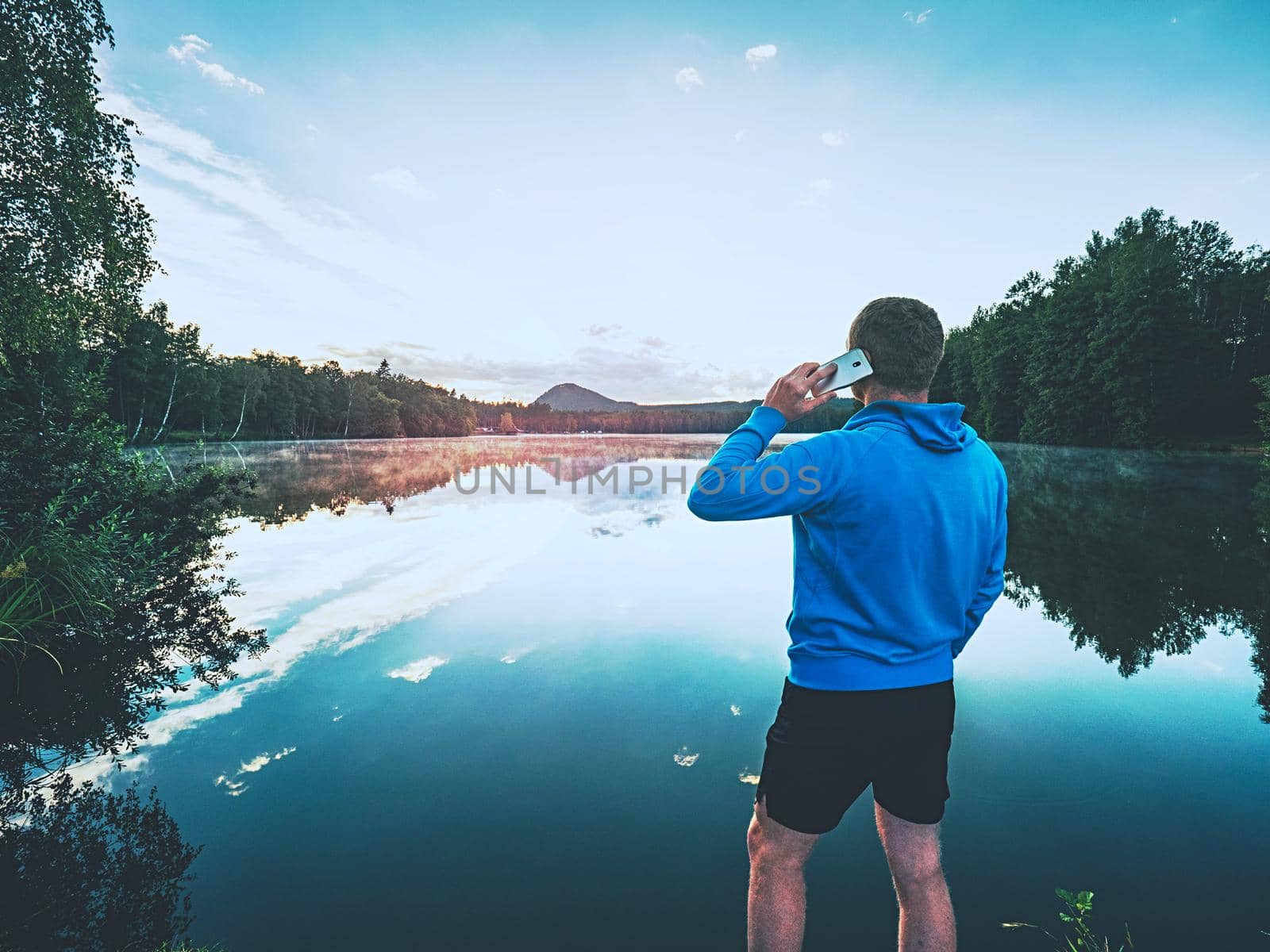 Man in blue sweatshirt makes a phone call at lake  by rdonar2