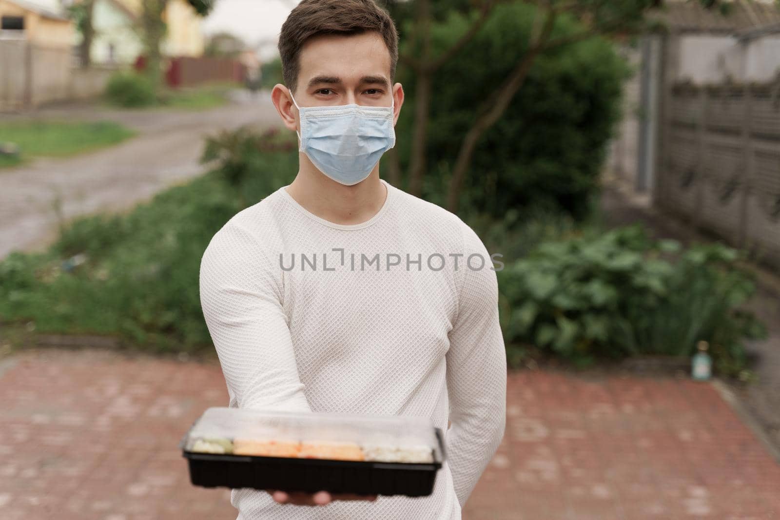 Sushi set in box healthy food delivery online service by car. Handsome man courier in medical mask gives sushi box to you. Japanese cuisine. by Rabizo