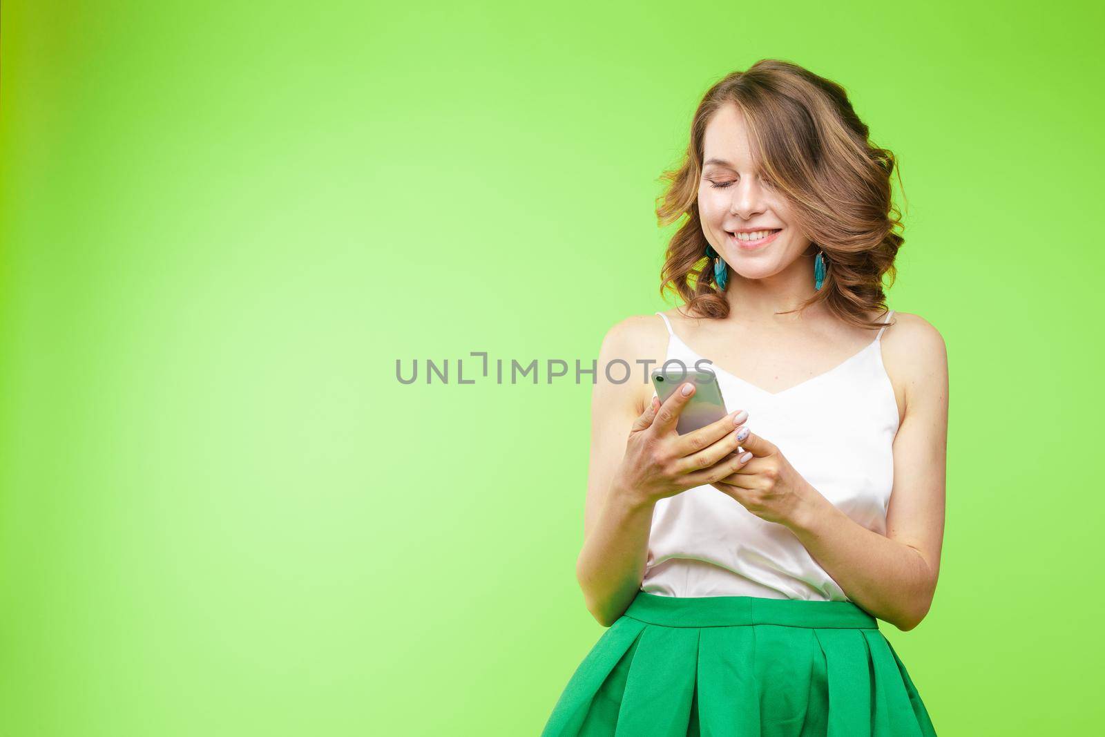 Studio portrait of beautiful caucasian brunette woman in patterned overall pointing at her smartphone with index finger. She is certain or sure about something. I know gesture.