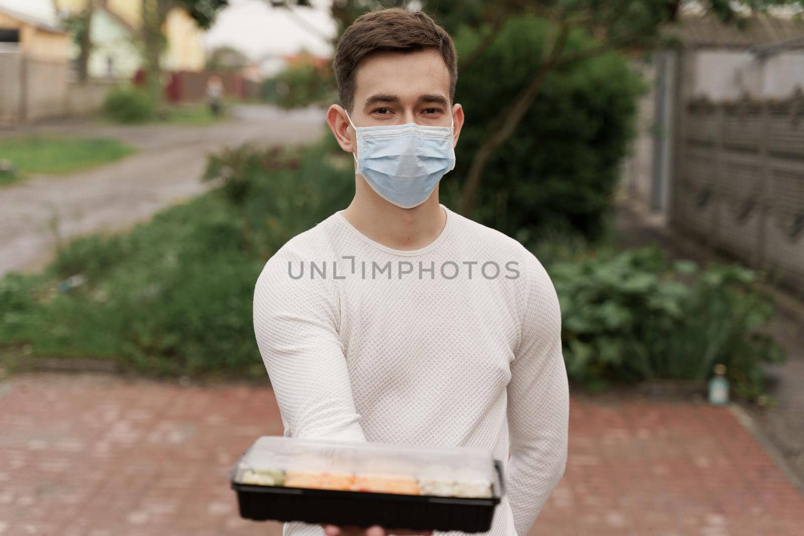 Sushi set in box healthy food delivery online service by car. Handsome man courier in medical mask gives sushi box to you. Japanese cuisine