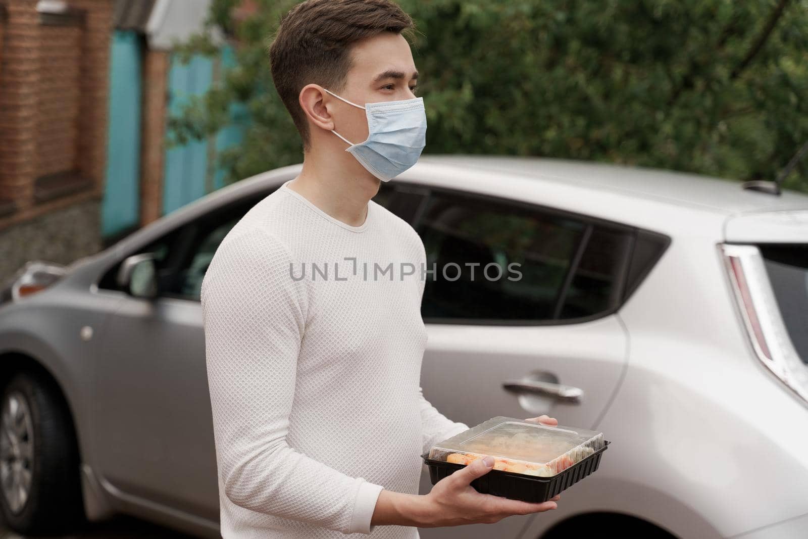 Sushi set in box healthy food delivery online service by car. Handsome man courier in medical mask gives sushi box to you. Japanese cuisine. by Rabizo