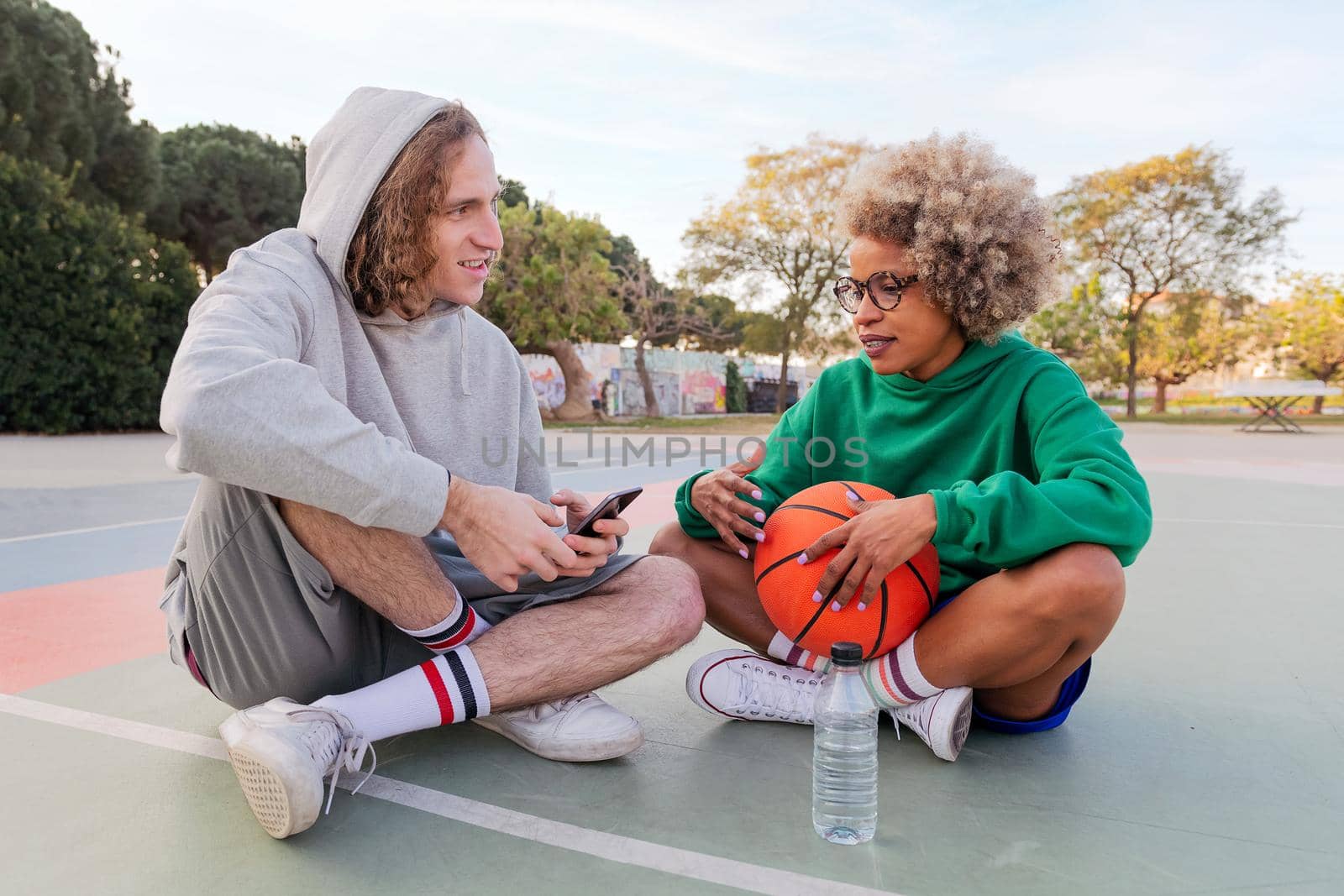 man and woman chat and share a good time sitting on the court after playing basketball at a city park, concept of friendship and urban sport in the street