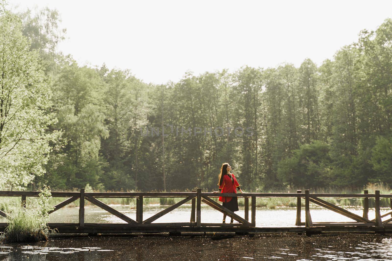 Georgian woman in red national dress with cross symbols. Attractive woman on the lake with forest background. Georgian culture lifestyle