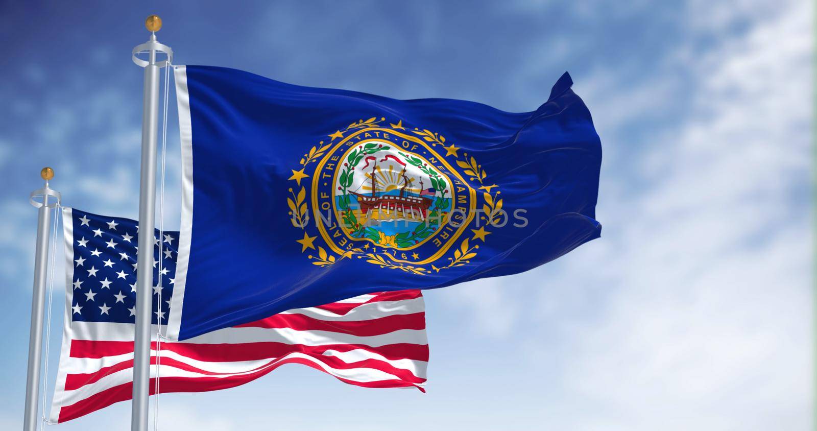 The New Hampshire state flag waving along with the national flag of the United States of America. In the background there is a clear sky. New Hampshire is a state in the New England region of the US