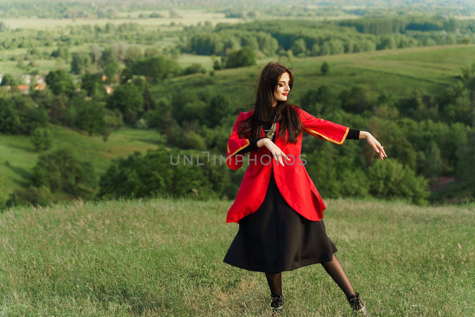 Georgian woman dances national dance in red national dress on the green hills of Georgia background. Georgian culture lifestyle.
