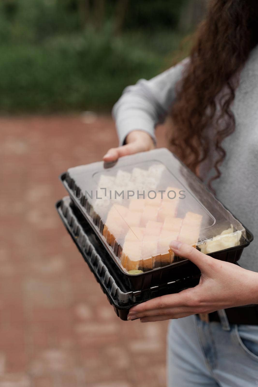 Close-up sushi in box healthy food delivery online service. Girl holds 2 sushi sets in hands. Japanese cuisine: rolls, soy sauce, wasabi