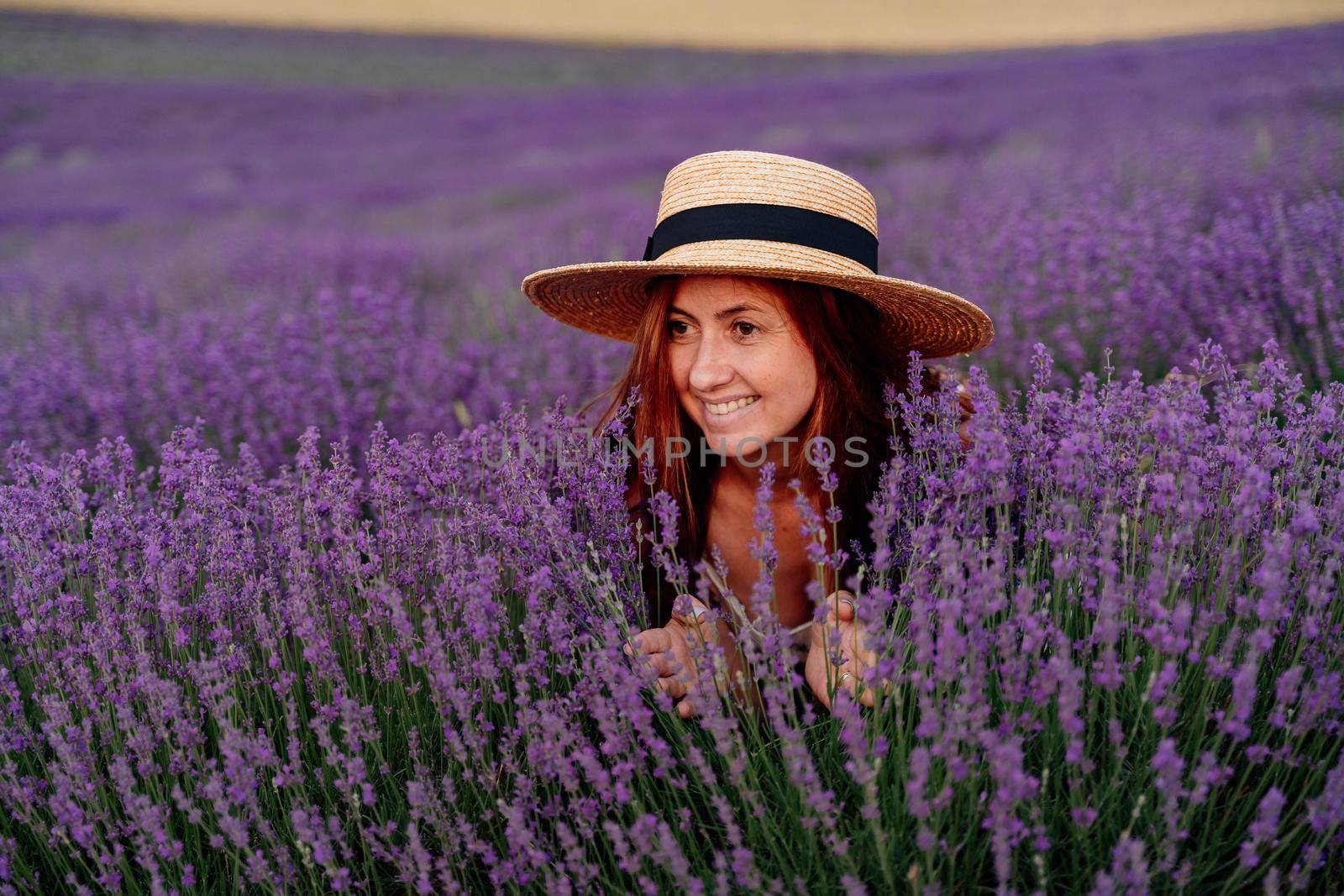 Close up portrait of a happy young woman in a dress on blooming fragrant lavender fields with endless rows. Bushes of lavender purple fragrant flowers on lavender fields
