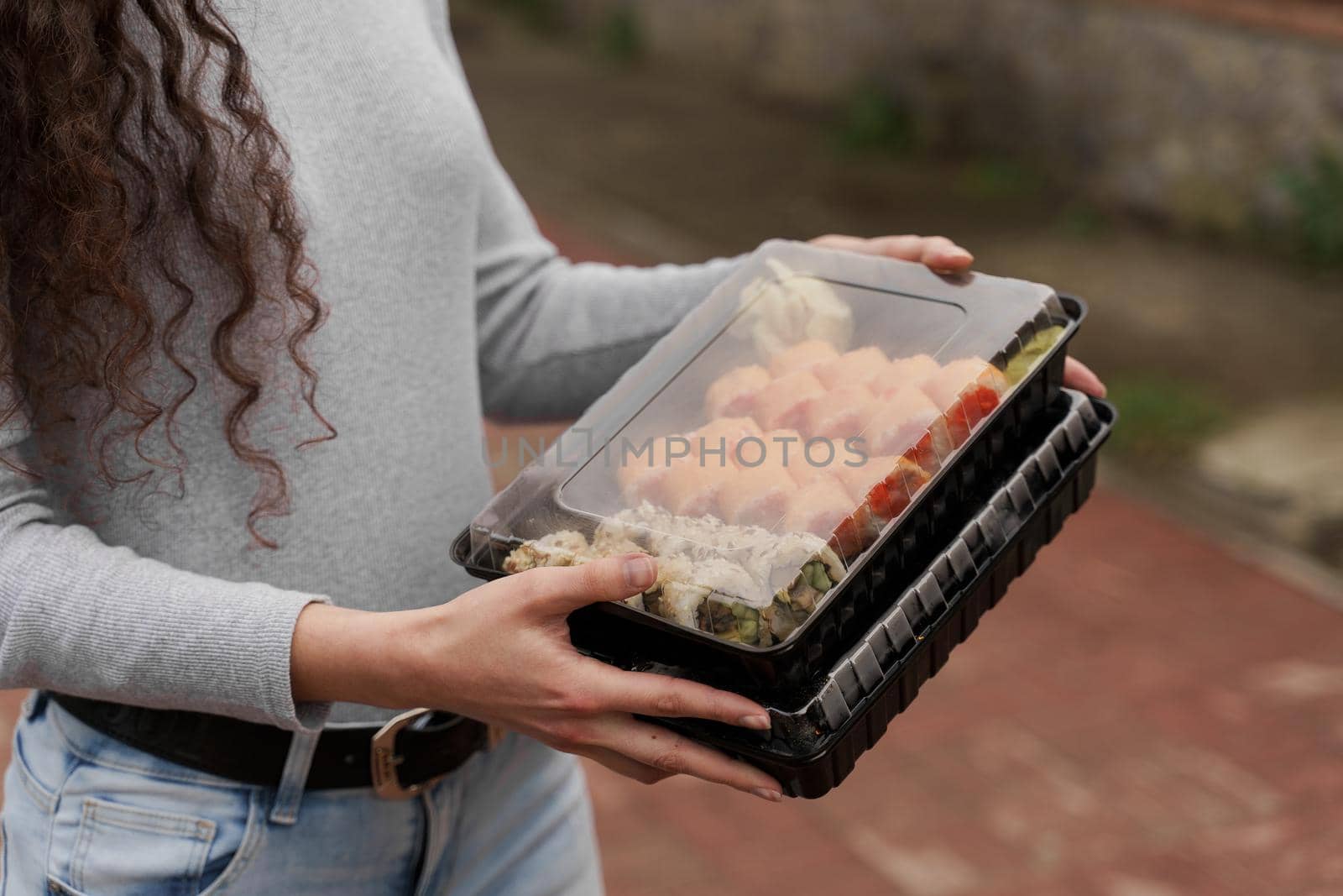 Close-up sushi in box healthy food delivery online service. Girl holds 2 sushi sets in hands. Japanese cuisine: rolls, soy sauce, wasabi