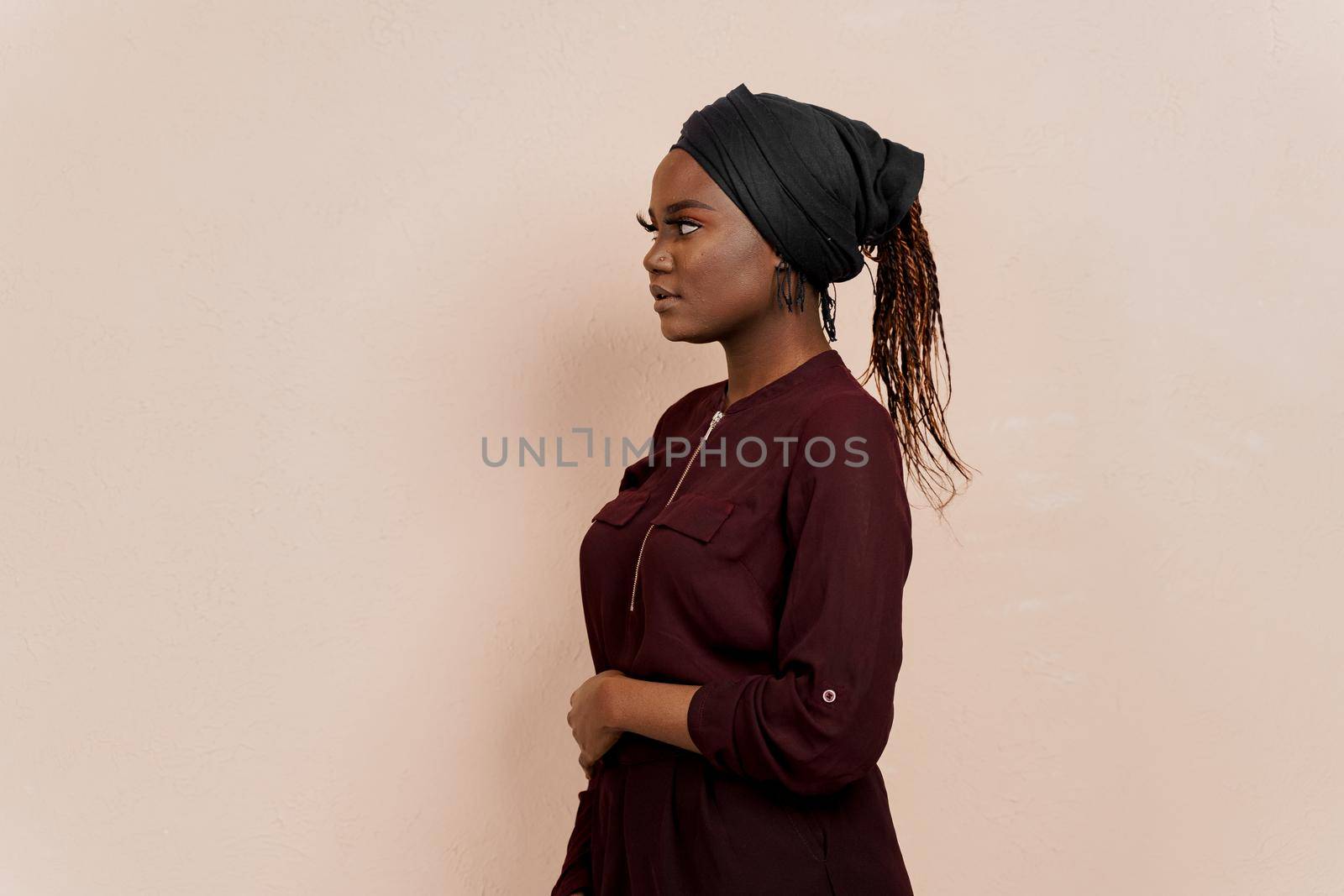 Muslim black girl looks left side. African woman weared in national dress and scarf isolated on peach background. by Rabizo