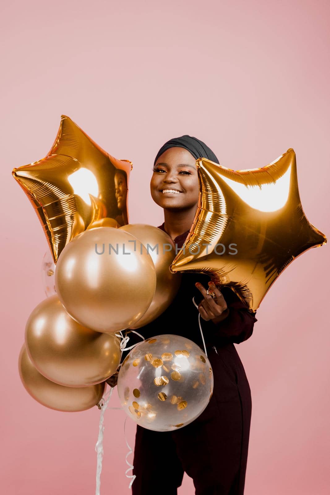 Muslim black girl with golden helium balloons smiles isolated pink background. African young woman celebrates her birthday. by Rabizo