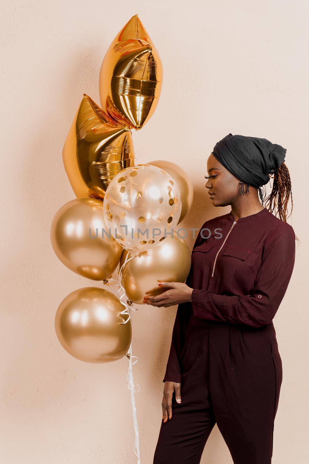 Muslim black girl with golden helium balloons isolated peach background. African young woman celebrates her birthday. by Rabizo