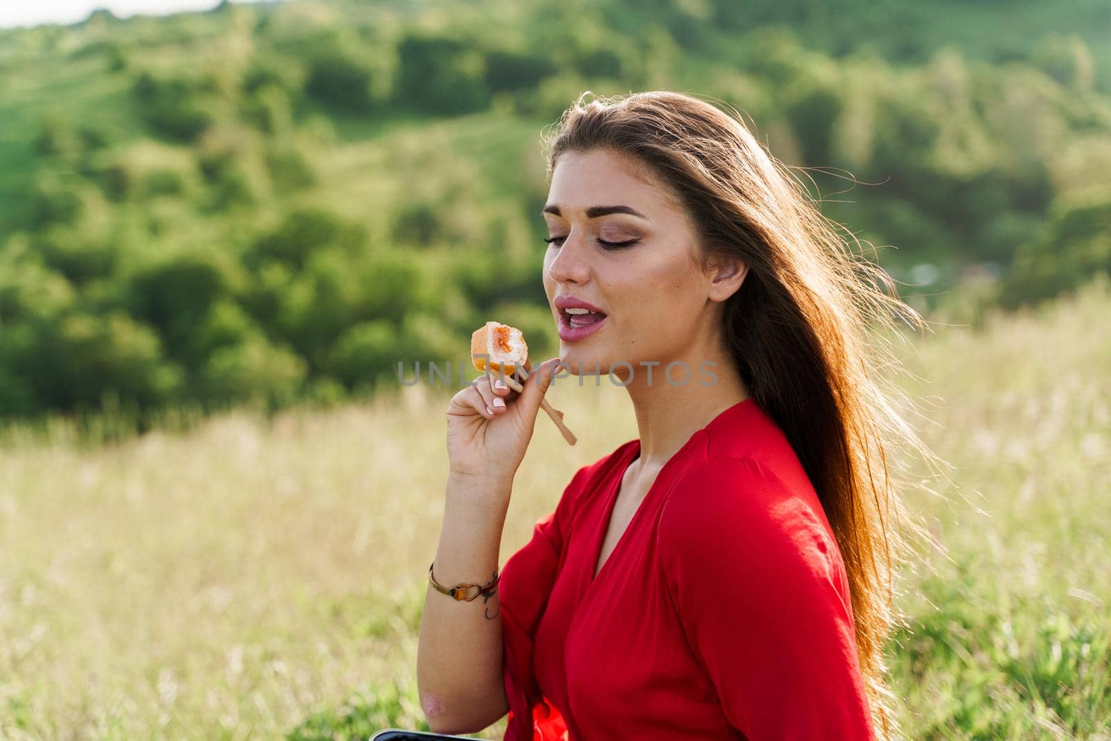 Sushi set and girl who reach out to bite sushi on green hills background. Food delivery service from japanese restaurant. Woman with blue eyes in red dress seats and eats sushi delivered by courier. by Rabizo