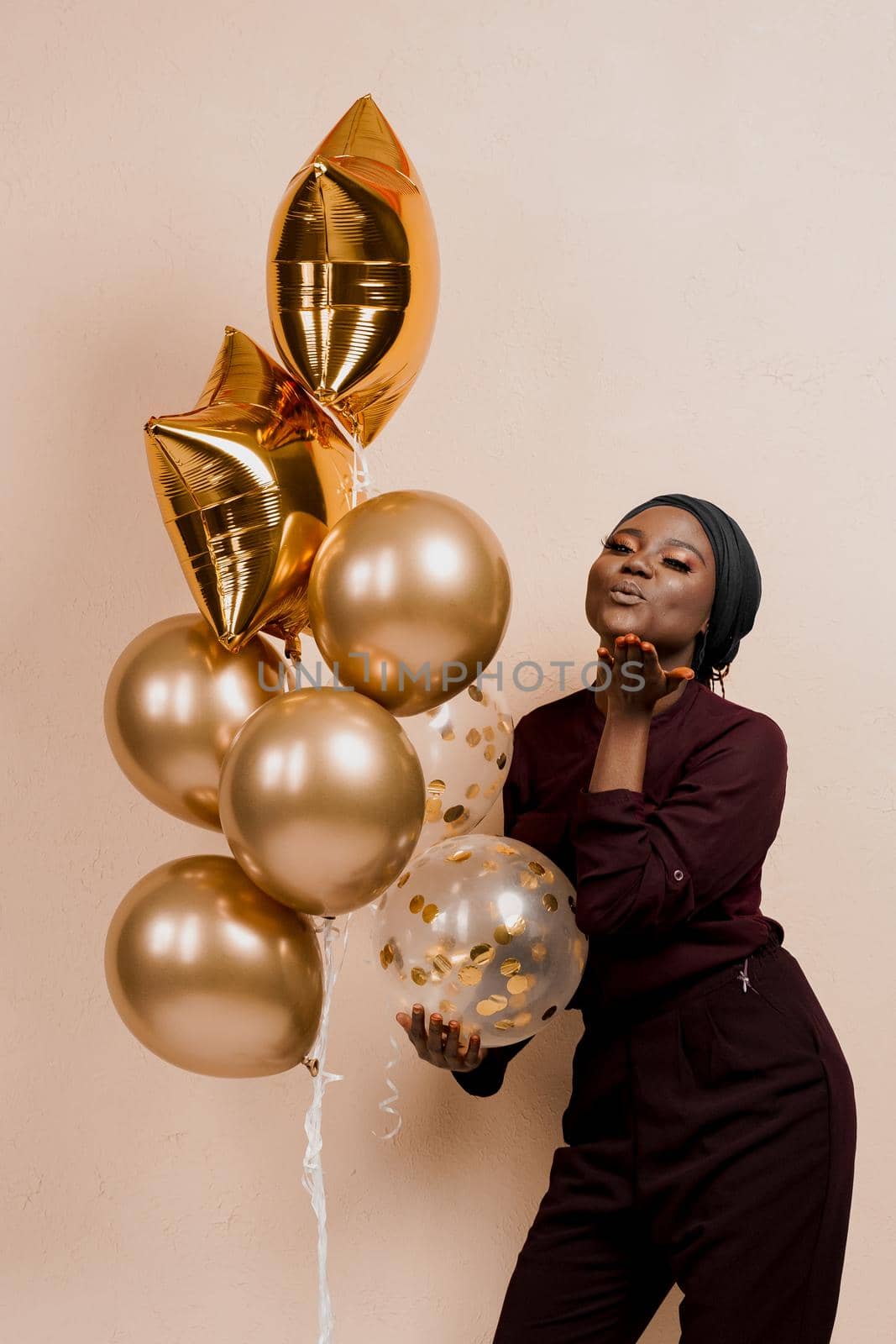 Black girl with golden ballons have a party and send a kiss. African woman celebrate new year. Happy emotions of muslim young woman. by Rabizo