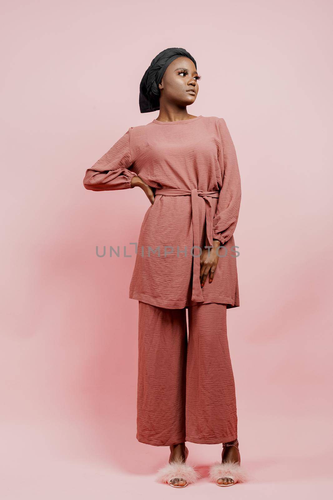 Muslim young woman weared in traditional dress and scarf isolated on pink background. Attractive and confident black model in studio