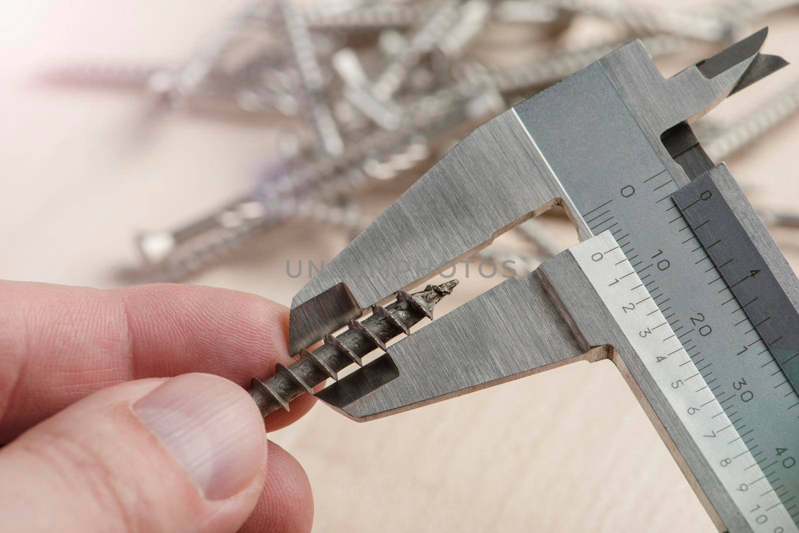 A man uses a caliper to measure the thickness of a screw with torx head. An accurate measuring device in the hands of a person against the background of screws scattered on the table.