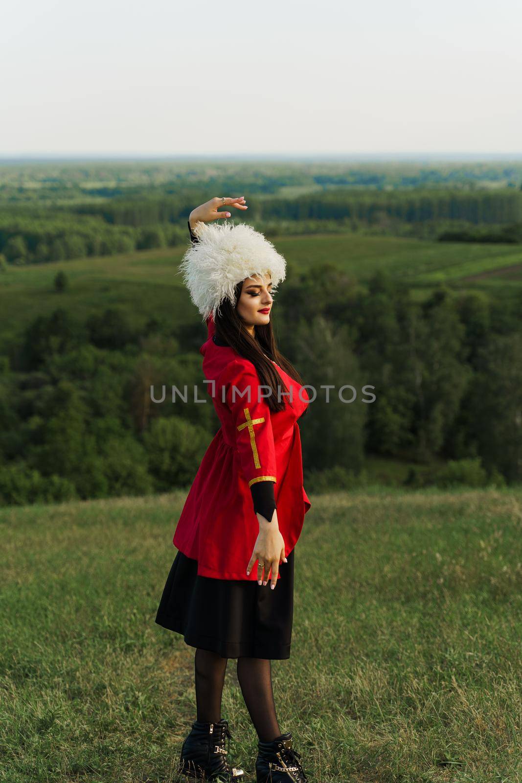 Georgian girl in white papakha and red national dress dances national dance named: rachuli, acharuli, osuri, shalaxo on the green hills of Georgia. by Rabizo