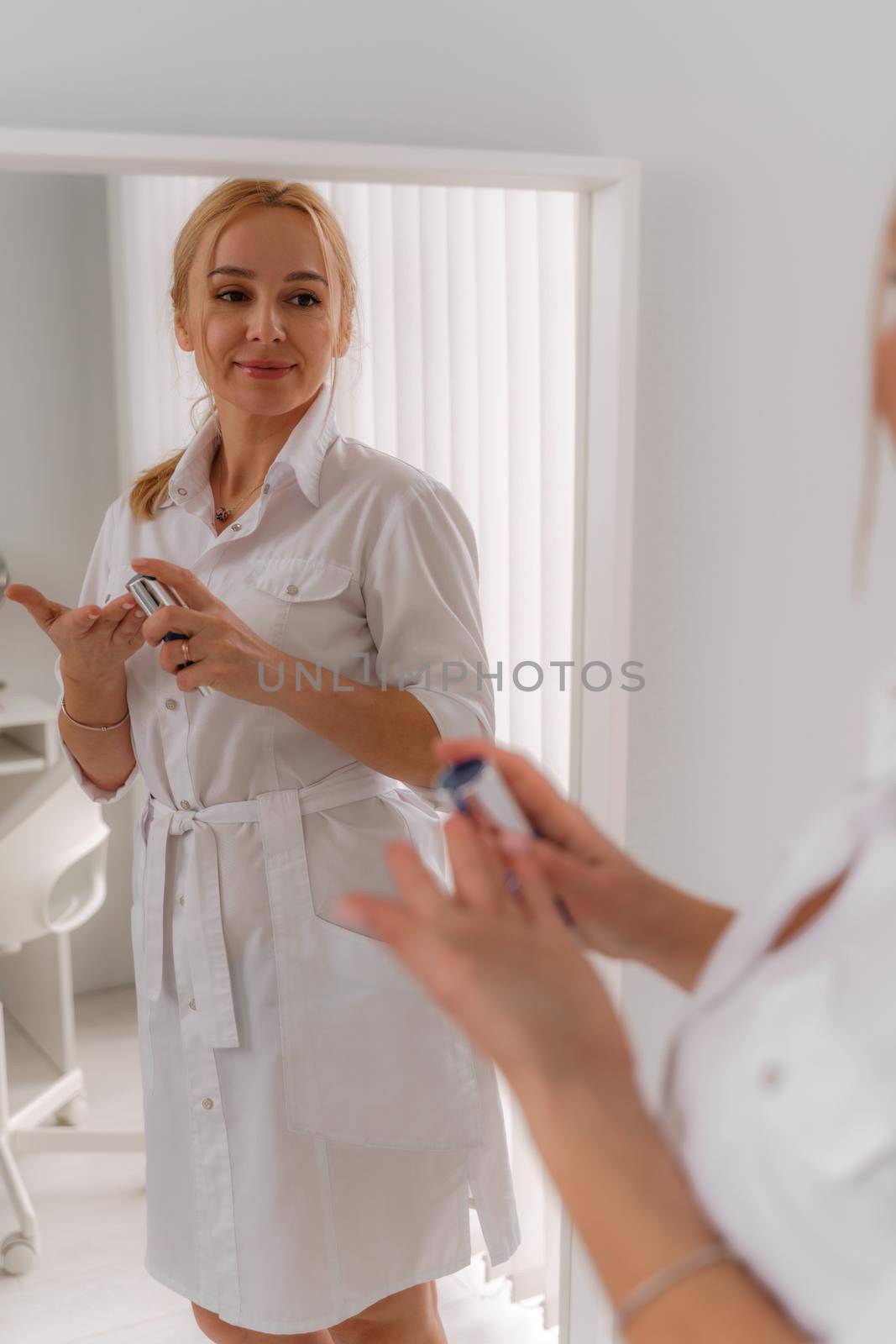 A blonde woman in white formal clothes looks out the window and is reflected in the mirror. On a white background