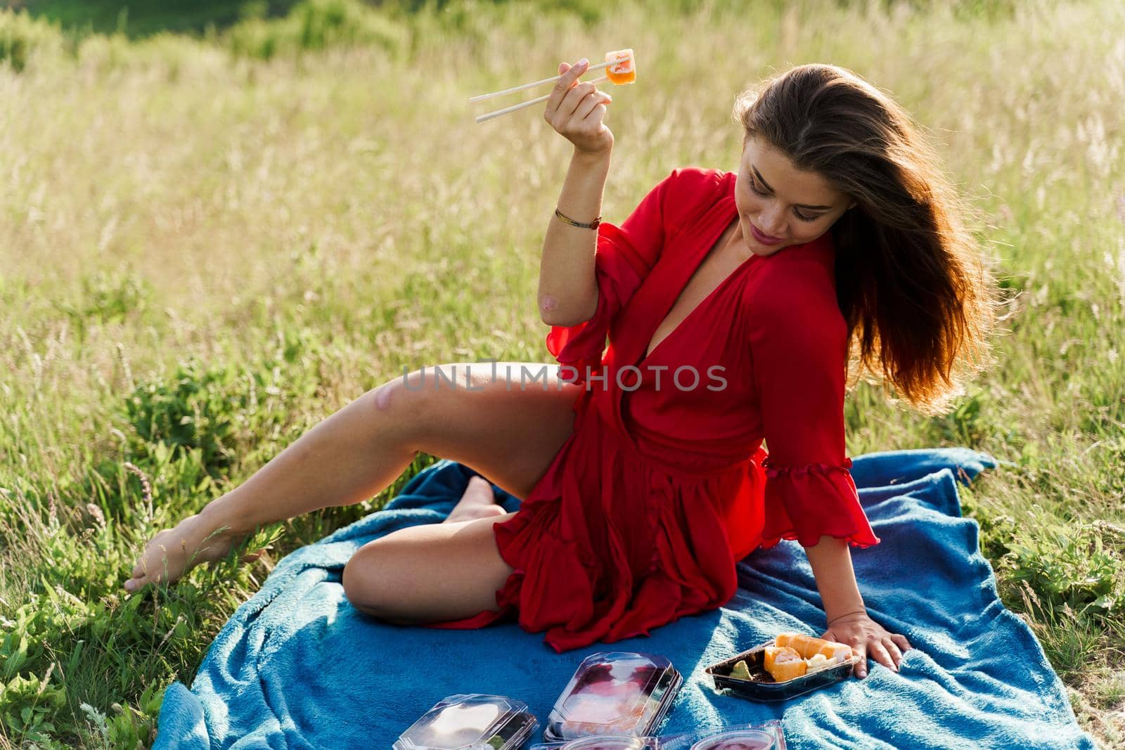 Sushi near lips of girl with blue eyes at picnic. Food delivery from japanese restaurant. Advert for social networks. Pretty girl eats sushi set in the park.