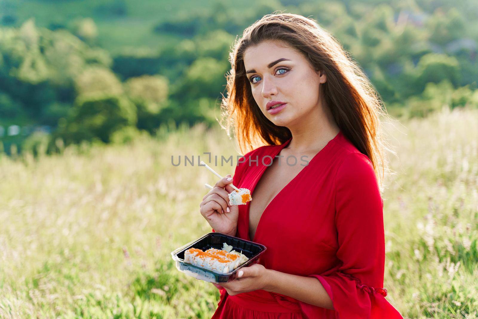 Sushi and sexy girl with blue eyes at picnic. Food delivery from japanese restaurant. Advert for social networks. Pretty girl eats sushi set in the park.