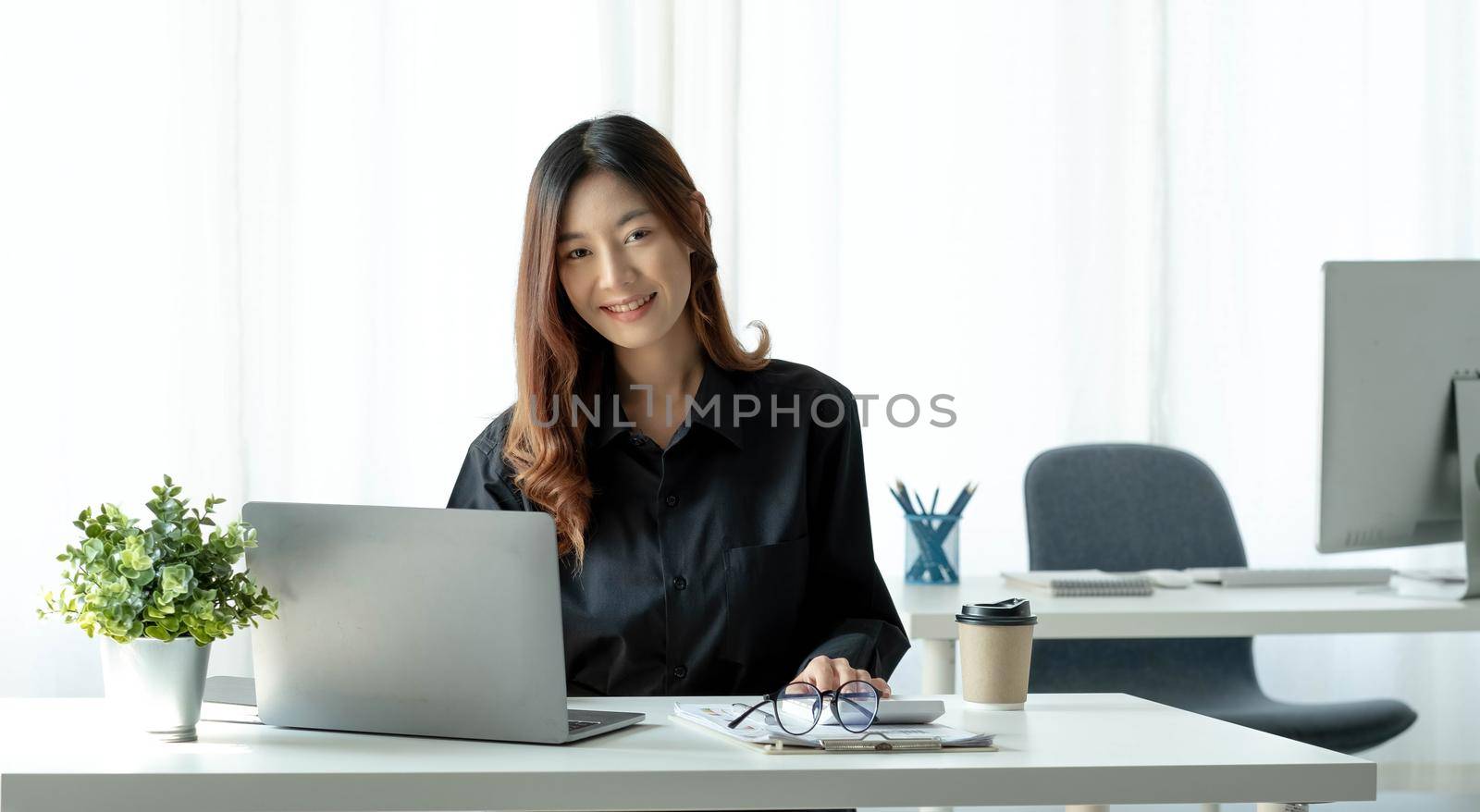 Charming Asian woman working at the office using a laptop Looking at the camera..