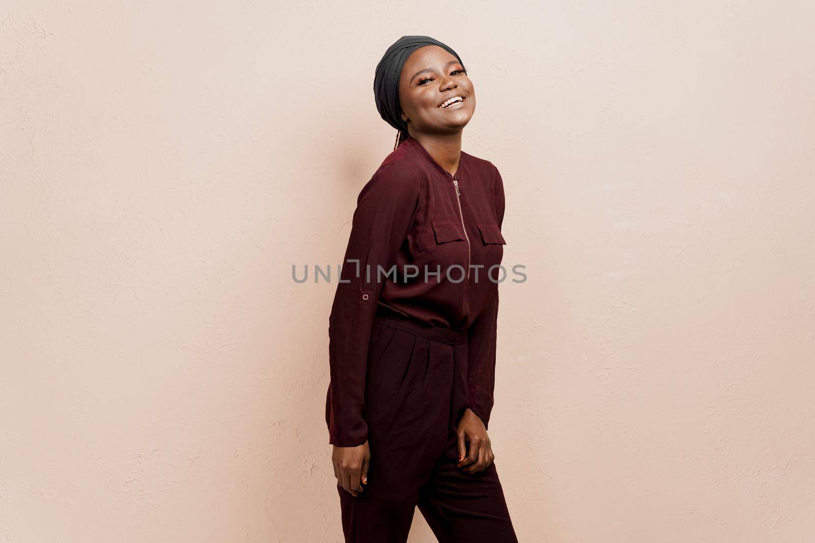 Muslim black girl smiles. African woman weared in national dress and scarf isolated on peach background. by Rabizo