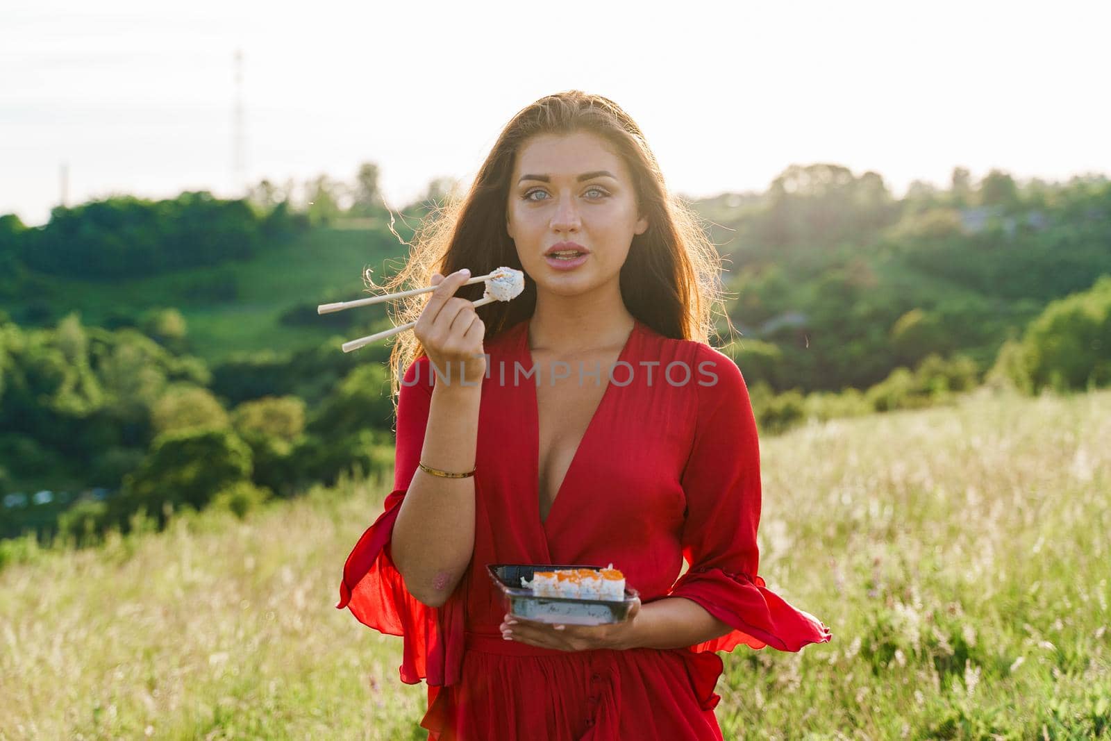 Sushi and sexy girl with blue eyes at picnic. Food delivery from japanese restaurant. Advert for social networks. Pretty girl eats sushi set in the park.