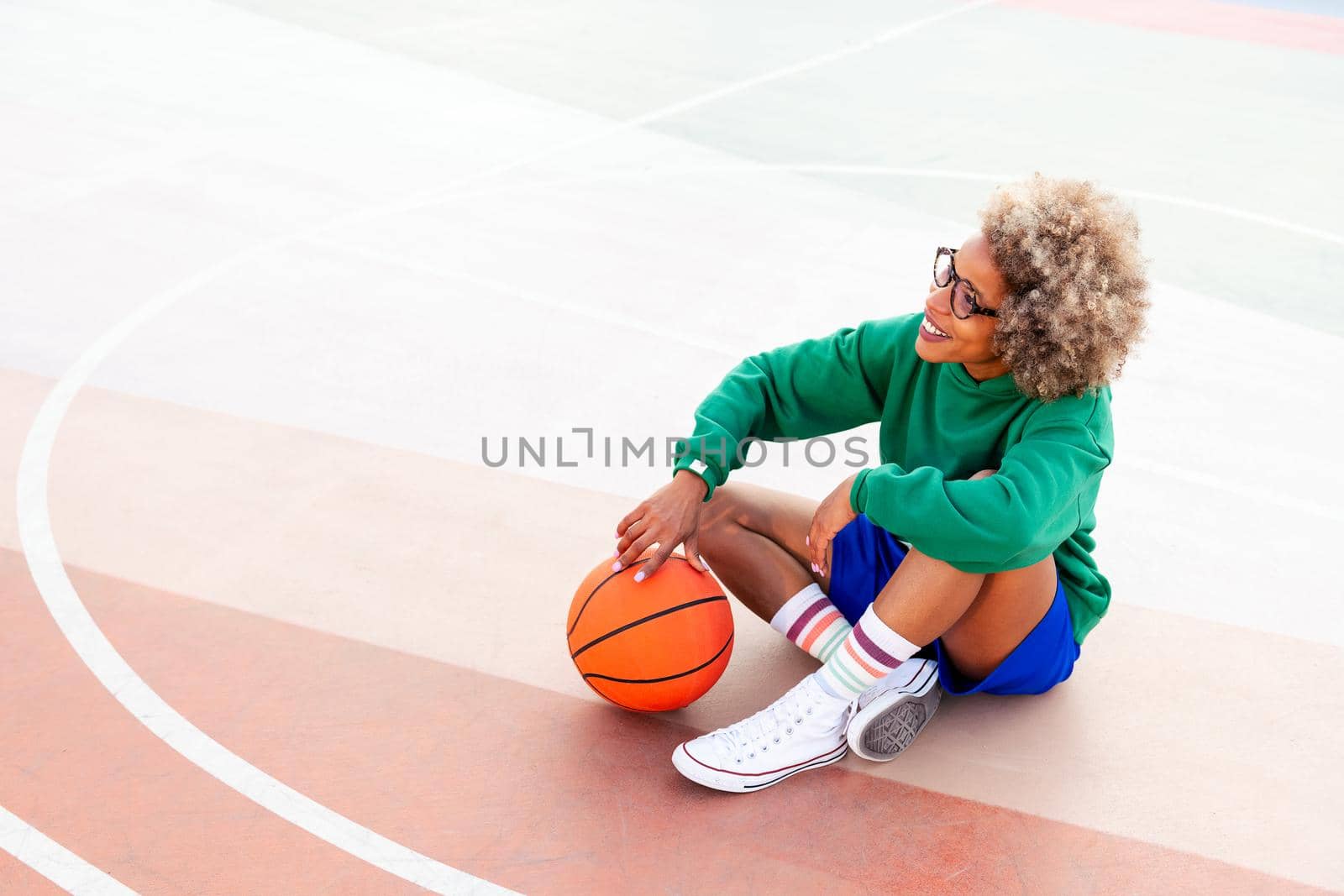 smiling latin woman resting sitting on the court after playing basketball, concept of urban sport outdoors, copy space for text