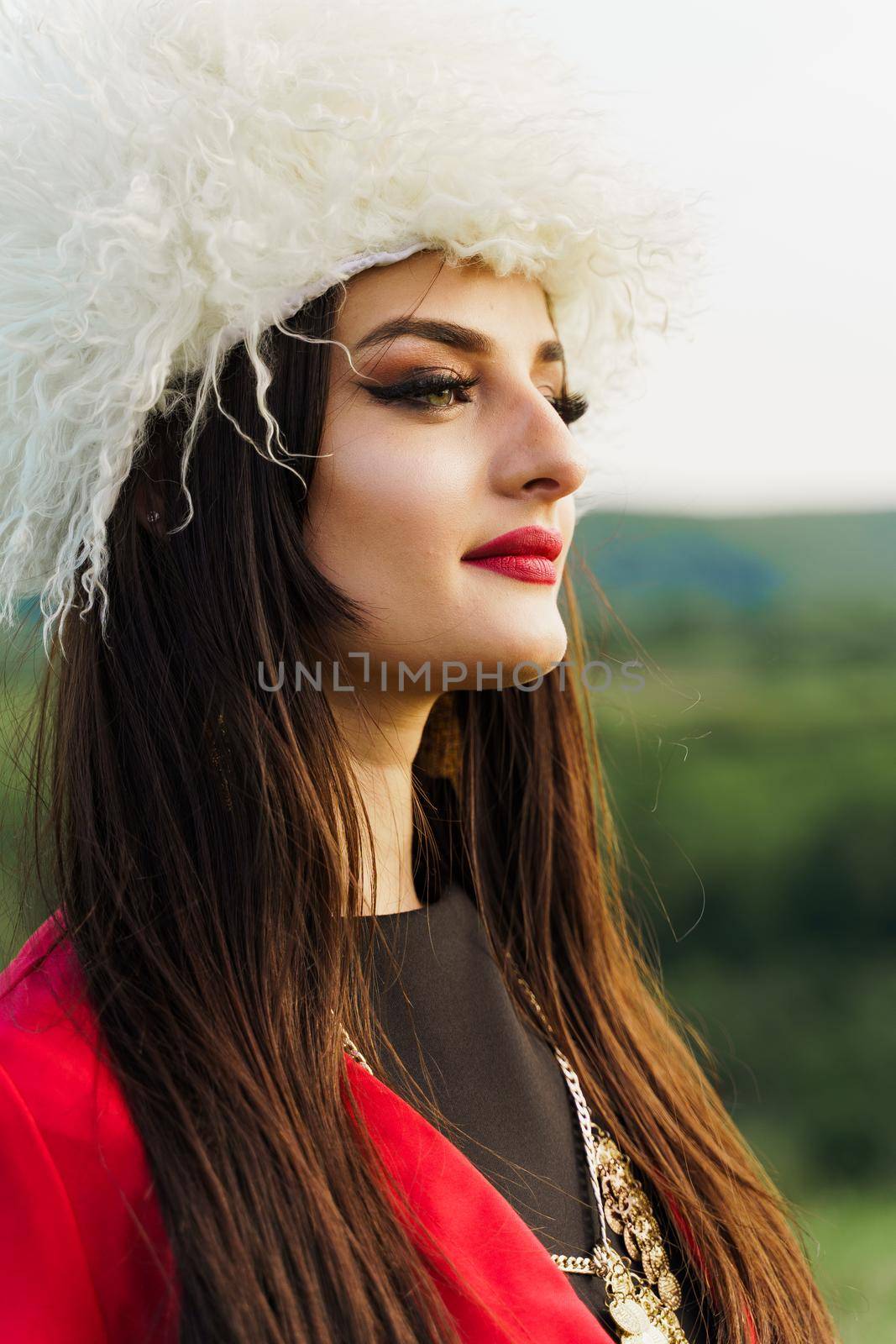 Georgian girl in papakha and red national dress with cross symbols. Attractive woman on the lake. Georgian culture lifestyle. Woman looks right side