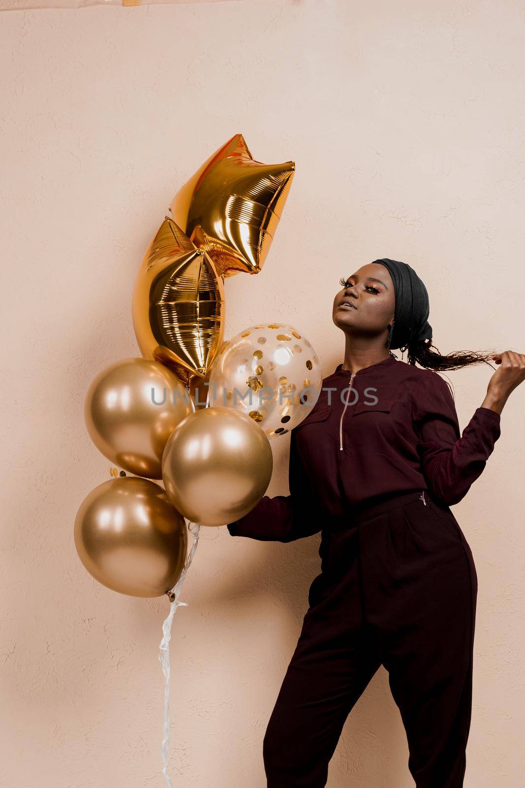 Black girl with golden ballons have a party and smile isolated on peach background. African woman celebrate graduation. Happy emotion of muslim young woman