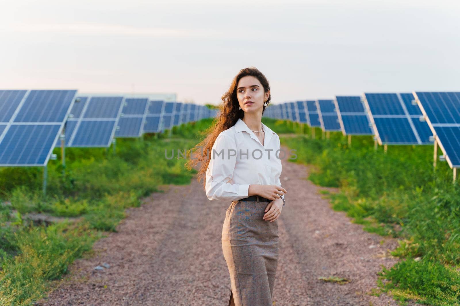 Girl stand between 2 Solar panels row on the ground at sunset. Free electricity for home. Sustainability of planet