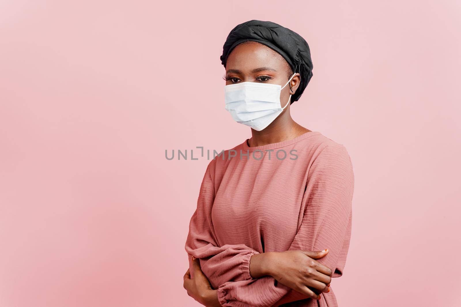Muslim girl in medical mask on the pink background. Portrait of african woman who sick coronavirus covid-19