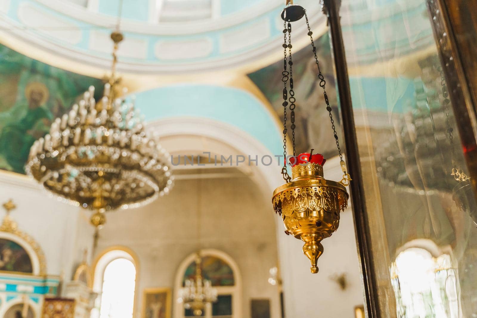 Gold censer with a red candlestick in the church. Big chandelier on the background. Church interior