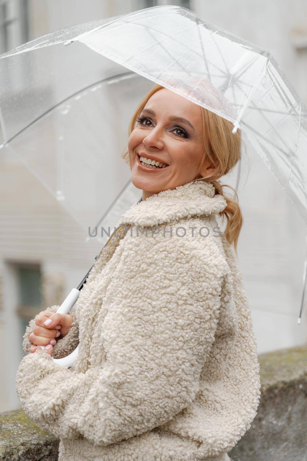 The blonde stands under a transparent umbrella during the rain. The fall season. Rear view. The woman is dressed in a black lace dress, her hair pulled back in a ponytail. by Matiunina