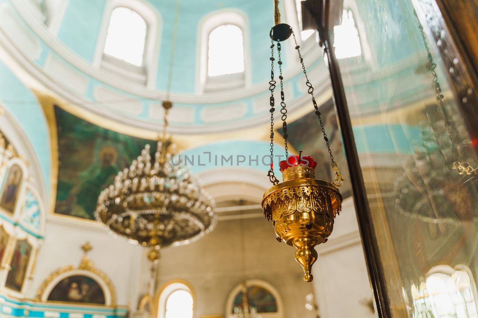 Gold censer with a red candlestick in the church. Big chandelier on the background. Church interior
