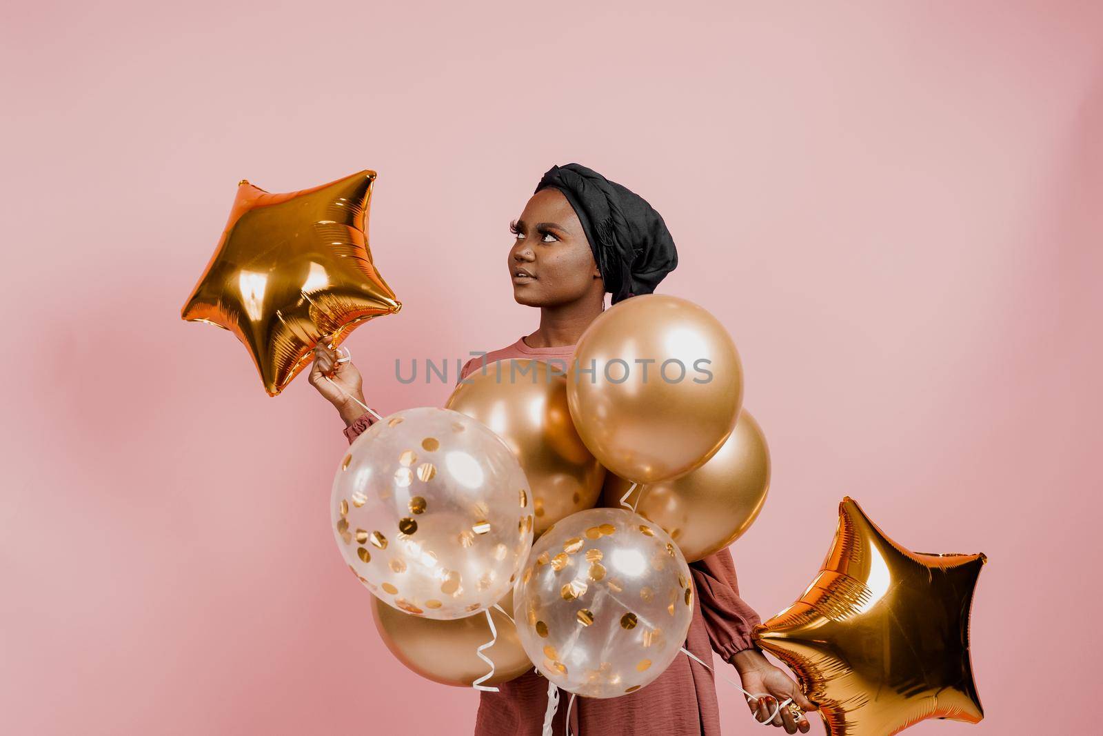 Eid al-Adha celebration. Muslim national holiday. Attractive girl with golden helium balloons isolated peach background.