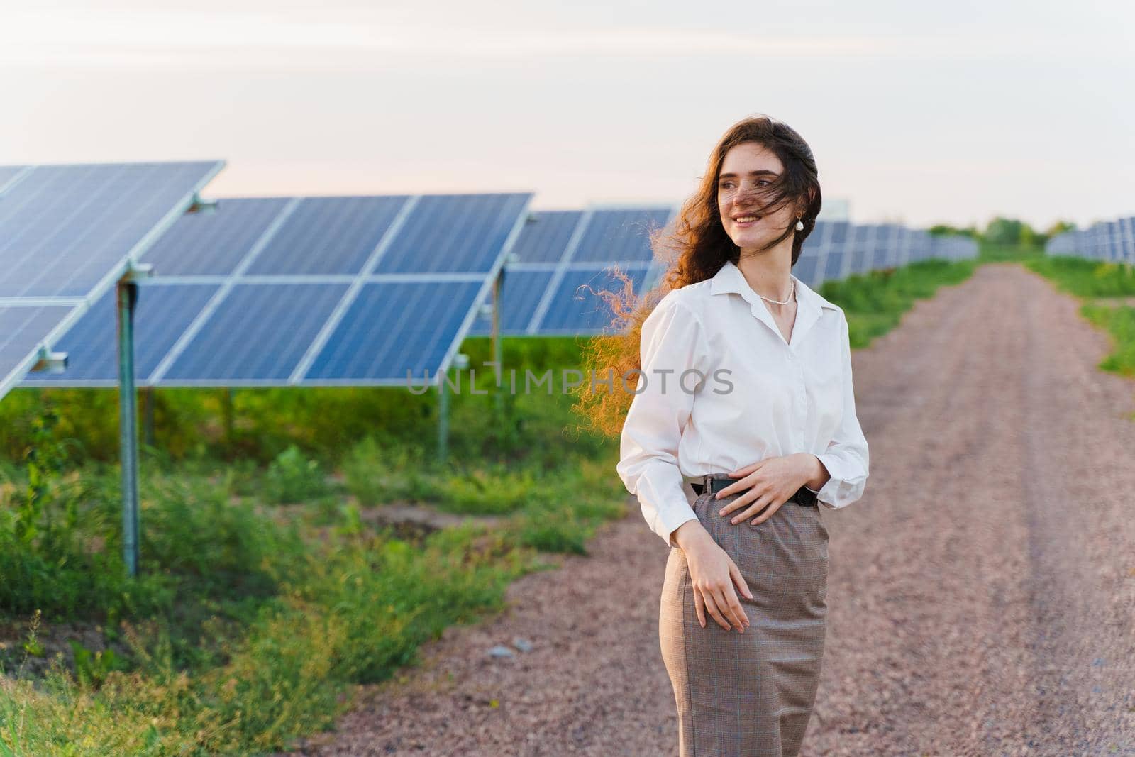 Girl stand between 2 Solar panels row on the ground at sunset. Free electricity for home. Sustainability of planet. by Rabizo