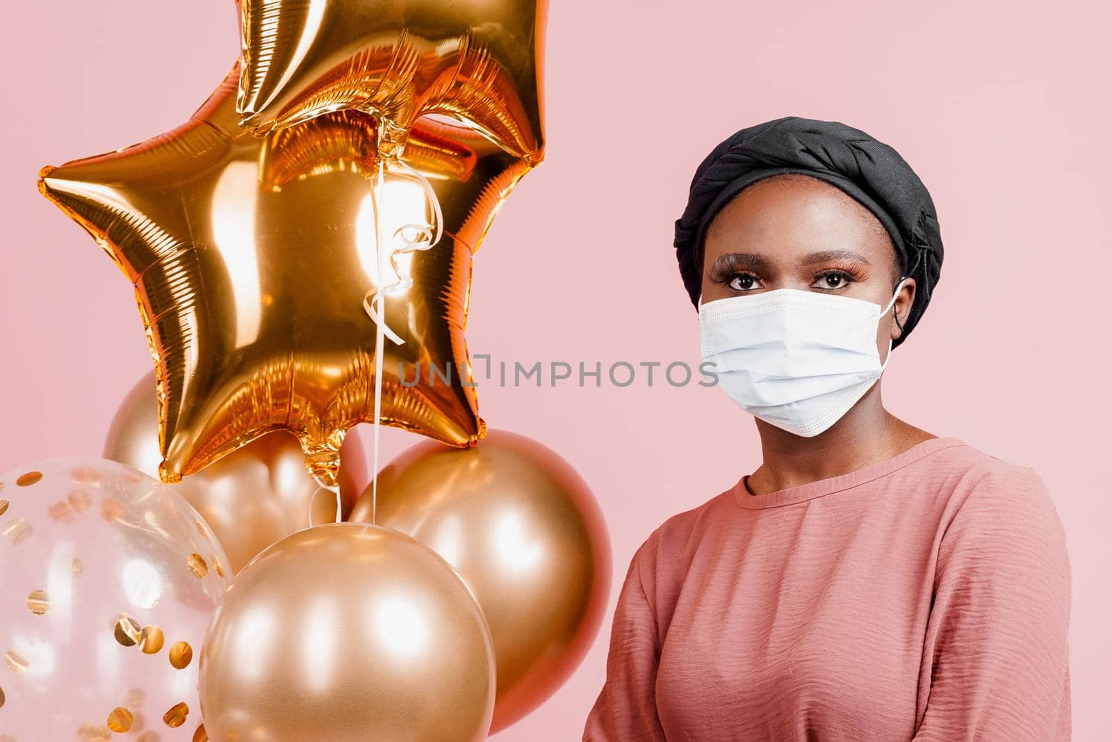 Muslim girl in medical mask on the pink background with baloons. Portrait close-up of african woman who sick coronavirus covid-19. by Rabizo