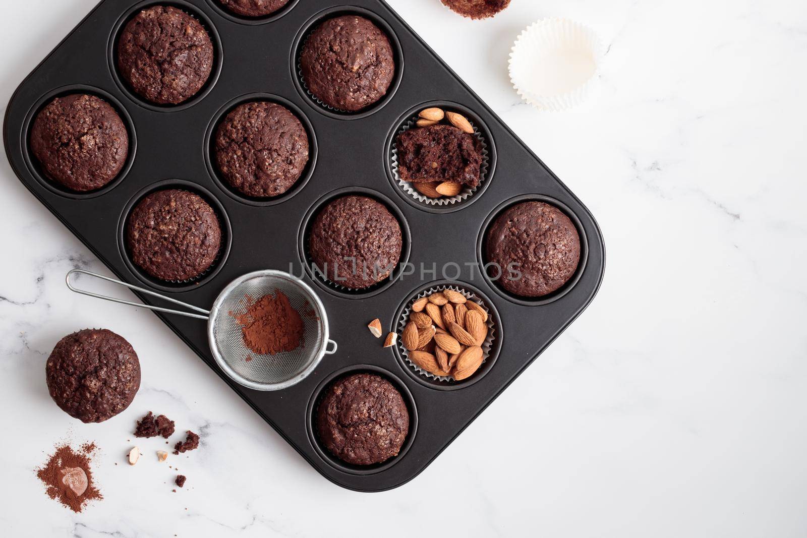 Freshly baked chocolate muffins in a baking pan on white table with ingredients