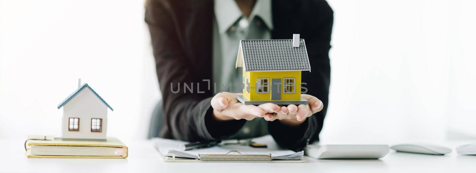 Miniature house in the hands of an Asian woman real estate agent home loan working at the office. by wichayada