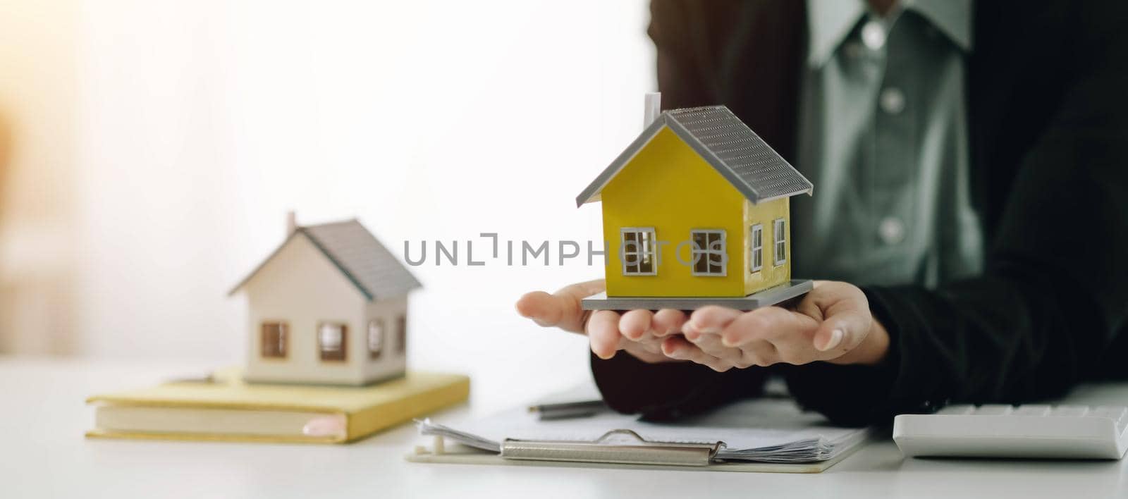 Miniature house in the hands of an Asian woman real estate agent home loan working at the office. Looking at the camera. by wichayada