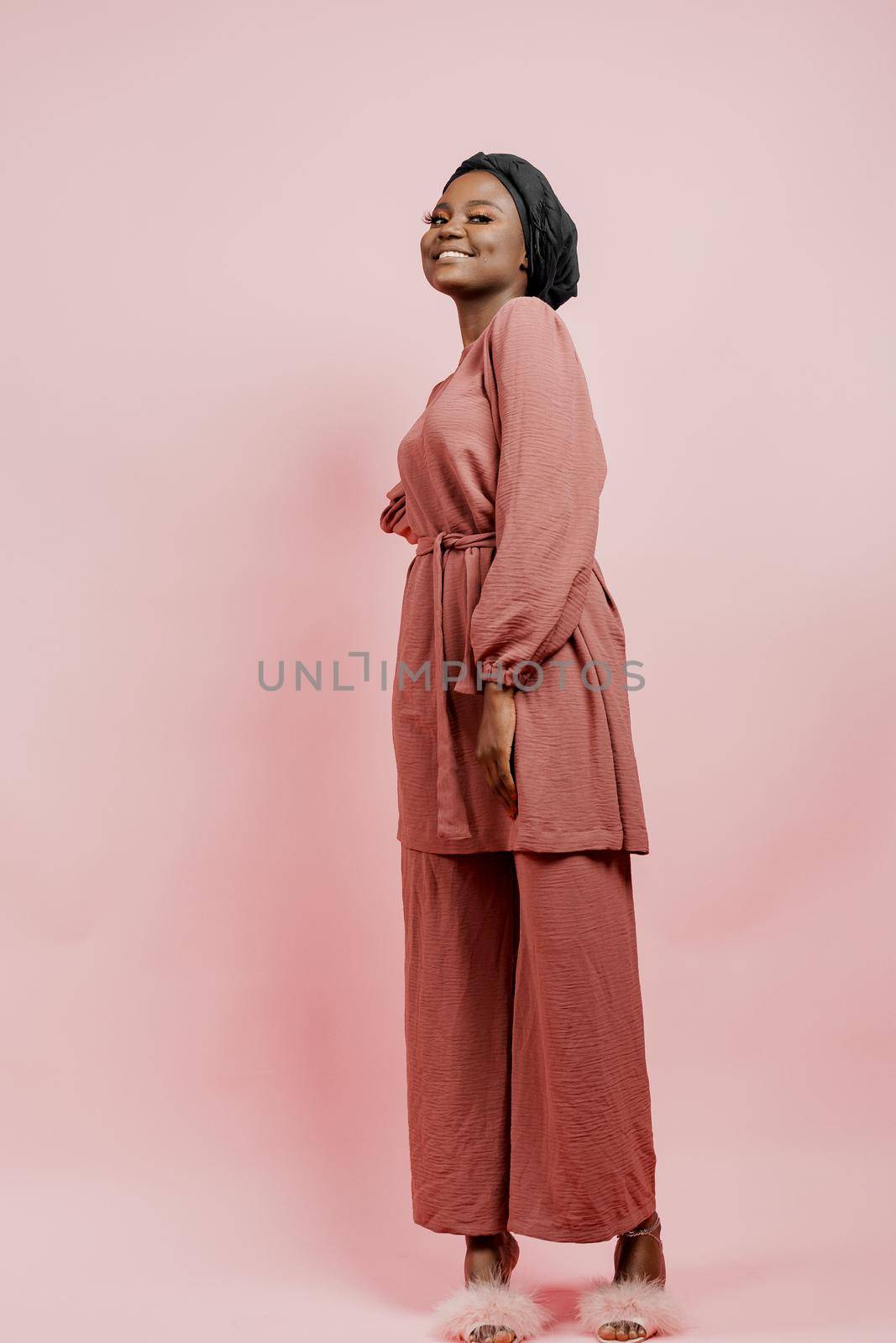 Muslim young woman weared in traditional dress and scarf isolated on pink background. Attractive and happy black model in studio