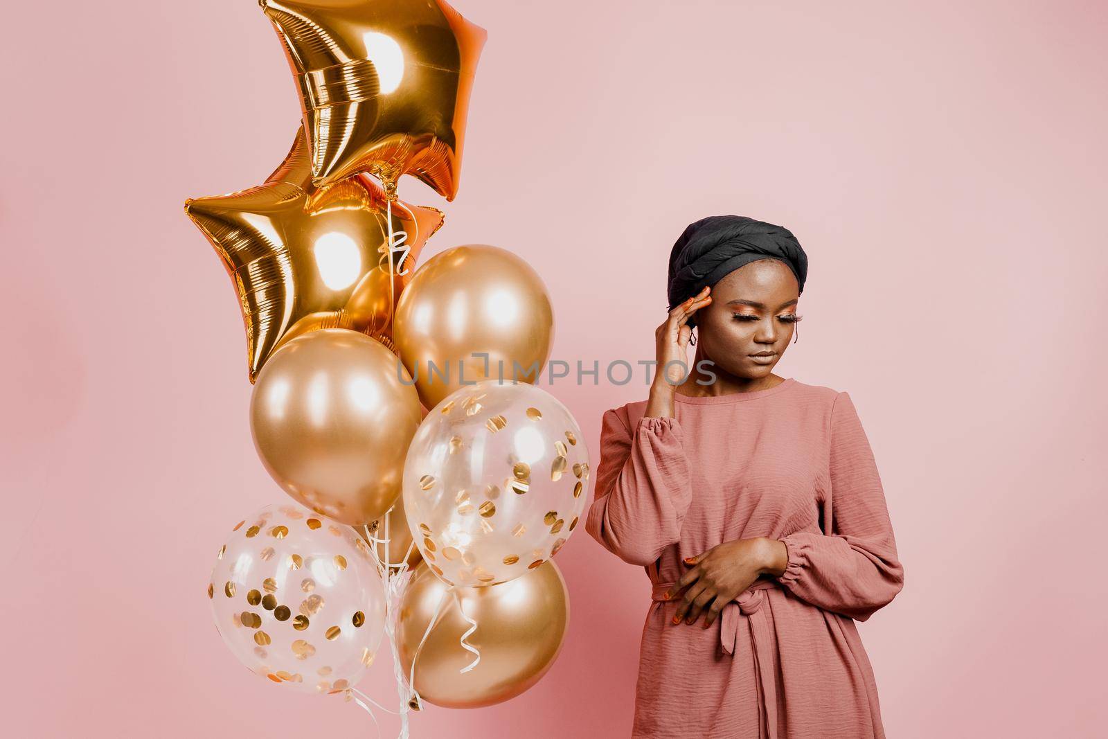 Eid al-Adha celebration. Muslim national holiday. Attractive girl with golden helium balloons isolated peach background.