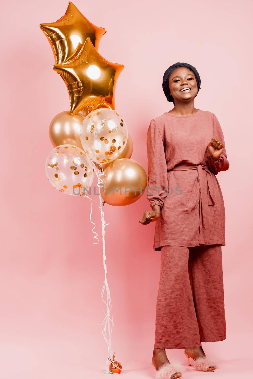 Eid al-Adha celebration. Muslim national holiday. Attractive girl with golden helium balloons isolated peach background