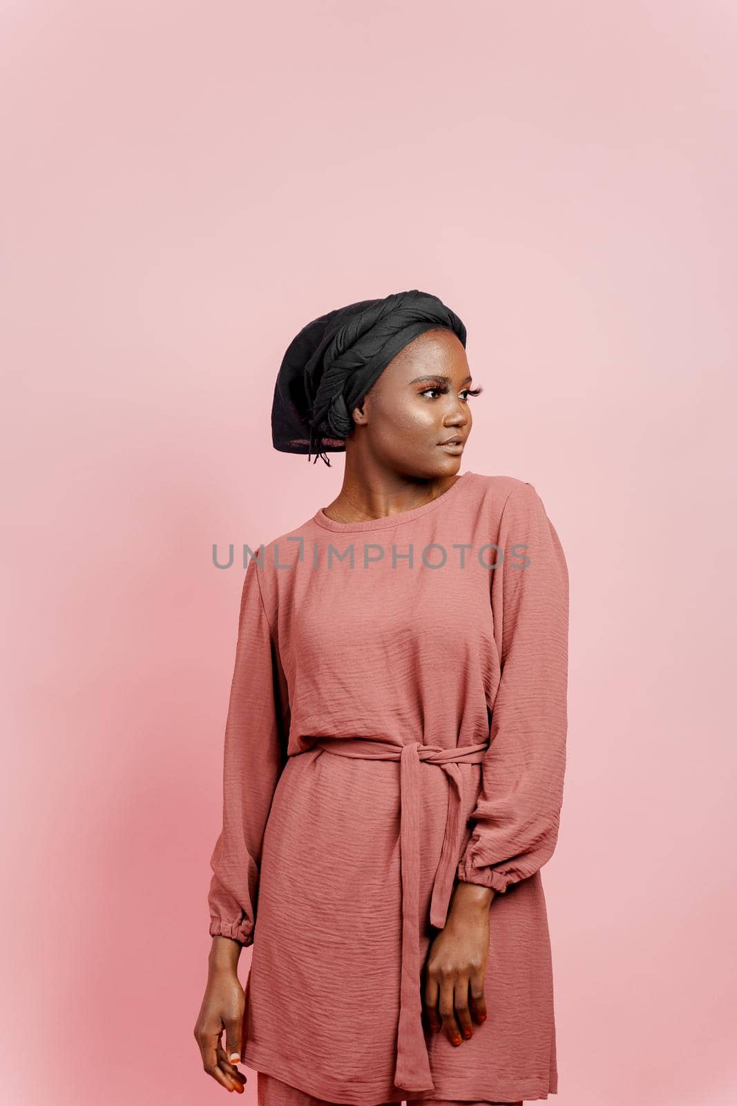 Muslim young woman weared in traditional dress and scarf isolated on pink background. Attractive and confident black model in studio. by Rabizo
