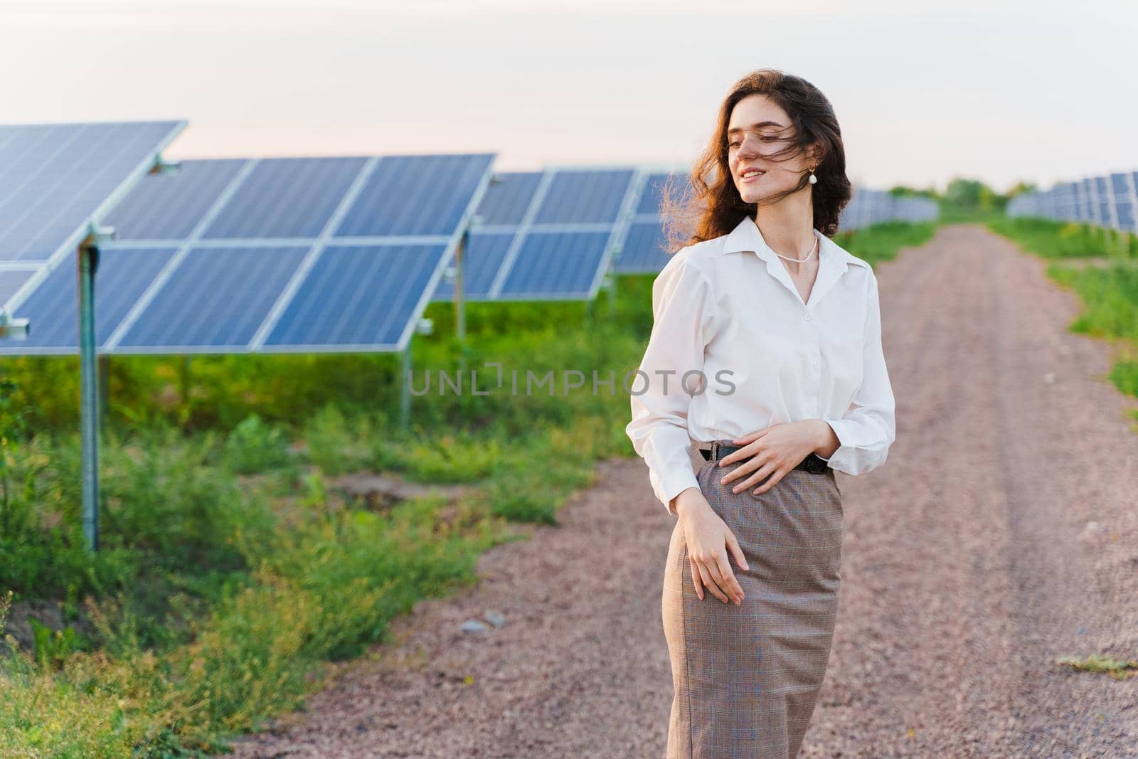 Girl stand between 2 Solar panels row on the ground at sunset. Free electricity for home. Sustainability of planet. by Rabizo