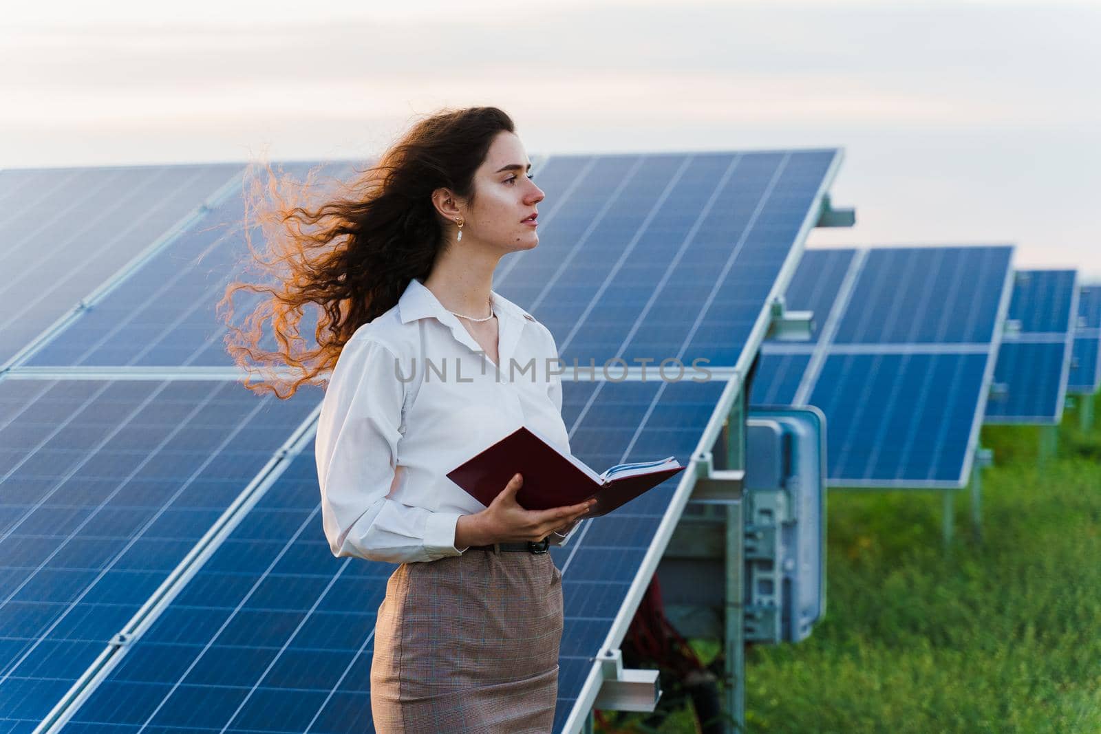 Model with solar panels stands in row on the ground. Girl dressed white formal shirt smiles on the power plant. by Rabizo