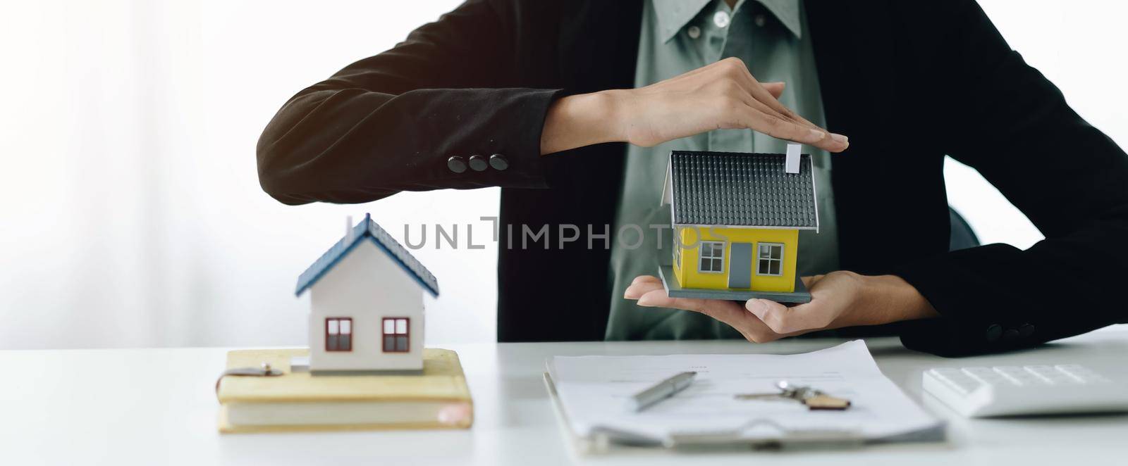 Miniature house in the hands of an Asian woman real estate agent home loan working at the office. by wichayada