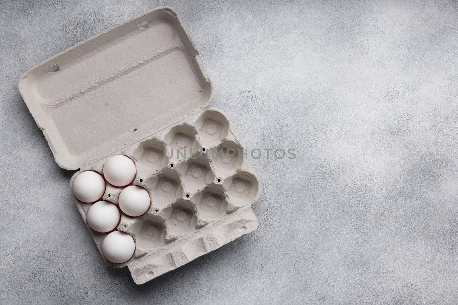 White eggs in a large paper container box top view on a neutral background