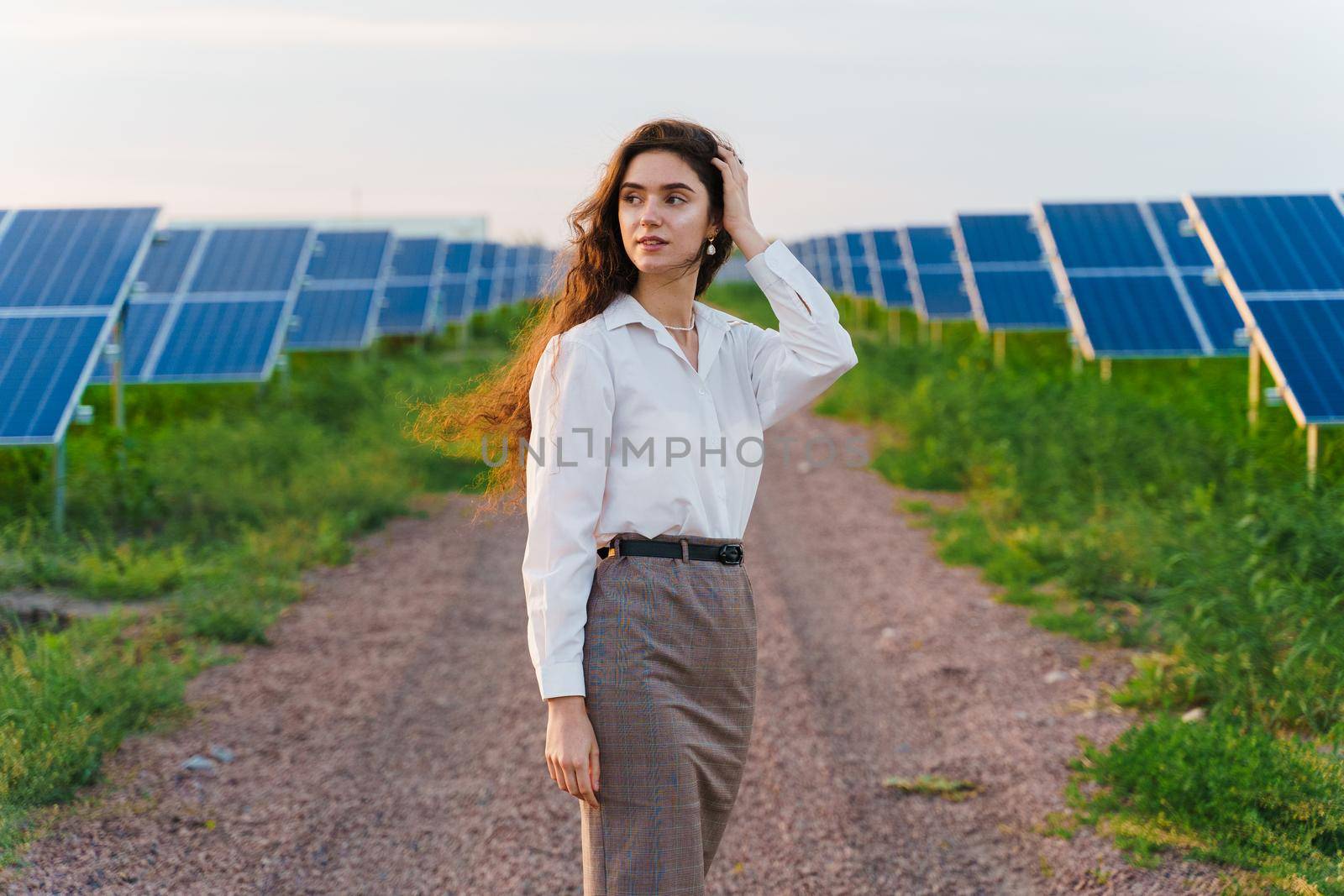 Girl stand between 2 Solar panels row on the ground at sunset. Free electricity for home. Sustainability of planet